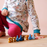 Ein Kind hat blaue "Regentropfen" Mandalasteine, braune Holzpilze Mandalas und einen rosa Mandalastein in einer Reihe aufgestellt.