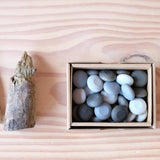 Das Mandala Legematerial Steine in verschiedenen Grautönen liegen in ihrer Kartonschachtel.