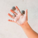 Ein Kind hält drei Mandala Steine in grau von Grapat zwischen den Fingern der offenen Hand.