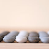 36 Stück Mandala Legematerial Steine in den drei verschiedenen Grautönen zu einem Quadrat mit sechs mal sechs Steinen aufgelegt, Nahaufnahme der ersten Reihe von vorne, alle anderen verschwimmen im Hintergrund.