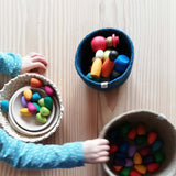 Ein Kind spielt mit verschiedenen Holzfiguren, die in drei verschiedenen Körben und Schalen vor ihm stehen.