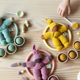 Türkis, Gelb und Altrosa Grüppchen im Pikler Spielraum: es sind immer Wichtel, Motorikring, Filzbälle in Holzschälchen von Grapat und kleine Spielfiguren zueinandern aufgelegt.