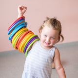 Ein Kind hat ganz viele bunte Motorikringe auf seinem rechten Arm aufgefädelt und hält den Arm in die Höhe.