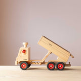 Der Fagus LKW Muldenkipper aus Holz seitlich, die Muldenkippe ist in der dritten Position, also in der steilsten Position und hinten öffnet sich schon die Mulde zum Abkippen. Im Führerhaus eine Spielfigur mit rotem Kugelkopf.