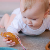 Ein Baby in Bauchlage hält den Beißring von Hevea in Panda Form in seiner rechten Hand und betrachtet die angebundene bunte Schnur.