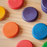 Coins von Grapat in Regenbogenfarben von ganz nahe, sodass die lasierte Farbe und die Holzmaserung gut zu sehen sind.