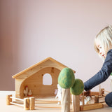 Ein Kind baut einen Bauernhof auf, mit kleinen Spielfiguren aus Holz und Filz.