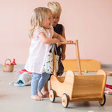 Zwei Kinder spielen mit dem Puppenwagen aus Holz von Lammetal, das Mädchen lacht stolz.