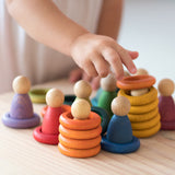Ein kleine Kinderhand, die mit bunten Holzringen von Grapat und den farblich passenden Holzspielfiguren spielt.