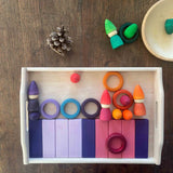 Auf einem Holztablett liegen bunten Holzbausteine, Holzringe und kleine Zwerge Spielfiguren aus Holz.