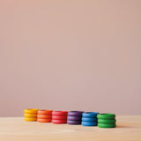 Grapat "Rings" Holzringe in 6 Farben des Regenbogens zu je drei Ringen und sechs Stapeln farblich sortiert aufgestellt.