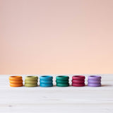 18 Stück Grapat "Rings" Holzringe in Erdtönen sind farblich sortiert zu je drei Ringen gestapelt nebeneinander aufgestellt.