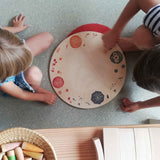 Zwei Kinder sitzen links und rechts von der runden Holzplatte "Seasons & Elements" von Grapat.