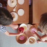 Zwei Kinder spielen Puppenküche, die Grapat "Seasons & Elements" Holzplatte dienst ihnen als Tablett für Töpfe, Körbe und Tassen.