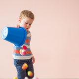 Ein Kind kippt bunte Häkelbälle von Kokomoo aus einem blauen Sandeimer ohne Henkel.