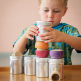 Ein Kind stellt ganz konzentriert eine Blechdose mit Schraubverschluss auf ein Bauwerk aus Dosen, Grapat Schälchen und Plättchen.