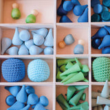 Ein Blick von oben auf den Tinker Tray Setzkasten von Grapat aus Holz befüllt mit blauen und grünen Mandalas, Holzfiguren und Häkelbällen von Kokomoo.