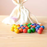 36 kleine Holzkugeln in Regenbogenfarben liegen vor dem Stoffsack, in dem sie von Grapat liebevoll verpackt geliefert werden.