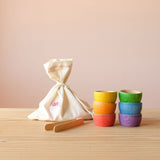 Grapat "Bowls and Marbles" Sortierspiel: die sechs Schälchen in Regenbogenfarben, daneben die kleine Holzzange, dahinter steht der Stoffsack, in dem die 36 Holzkugeln aufbewahrt werden.