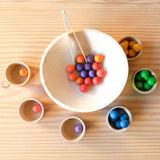 Grapat "Bowls and Marbles" Sortierspiel: die 36 Kugeln sind entweder bereits in die farblich passenden Schälchen sortiert oder liegen noch in der Mitte in einer großen Holzschale mit der kleinen Holzzange zum Greifen.
