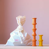 Ein zugebundener Stoffsack mit Grapat "Spools" Spulen aus Holz, in 6 bunten Regenbogenfarben, daneben zwei Stapel mit 5 orangen und 2 gelben Holzspulen in unterschiedlichen Formen.