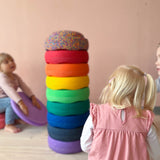 Stapelstein Regenbogen Classic 8 Steine aufgestapelt, ganz oben sitzt ein Confetti Stein auf dem Turm, zwei Kinder sehen den großen Stapelsein Turm staunend an.