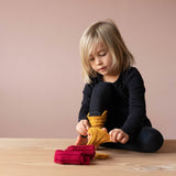 Ein Kind zieht sich die dottergelben Stulpen von Kokomoo an. Vor ihm liegt ein Paar rote Stulpen zusammen gefaltet.