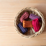 Fünf Paar Stulpen von Kokomoo in den Farben Kürbis, Malve, Fuchsia, Rosenholz und Lavendel liegen in einem Korb.