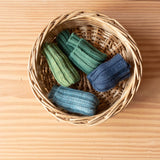 Vier Paar Stulpen von Kokomoo in den Farben Nachtblau, Gletscher, Waldgrün und Limette liegen in einem Korb.