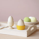 Das kleine Holztablett von Kokomoo mit einem gelben Holzbecher mit Holzei, einem Holzeierbecher mit Holzei und einem Holzlöffel, dahinter eine Holzschale mit Häkelbällen - Frühstück in der Puppenküche.