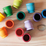 Grapat "Mates" Töpfchen aus Holz in 12 Farben liegen kunterbunt verteilt am Boden.