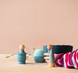 Blaue Grapat Spielmaterialien aus Holz mit einem hellblauen Häkelball von Kokomoo und einem dunkelblauen Körbchen. Eine Kinderhand greift nach dem Ball.