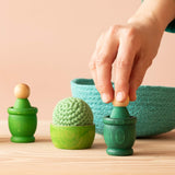 Grüne Grapat Spielmaterialien aus Holz mit einem grünen Häkelball von Kokomoo und einem grünen Körbchen. Eine Hand greift nach einem Grapat Nin.
