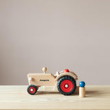 Der Fagus Traktor aus Holz von der Seite, eine Spielfigur sitzt im Traktor, eine steht daneben.
