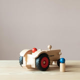 Der Fagus Traktor aus Holz von schräg hinten, sodass die Anhängerkupplung zu sehen ist, eine Spielfigur sitzt im Traktor, eine steht daneben.