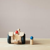 Der Fagus Traktor aus Holz von hinten, die Anhängerkupplung ist zu sehen. Eine Spielfigur sitzt im Traktor, eine steht daneben.