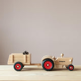 Der Fagus Traktor aus Holz von der Seite, ein kleiner Anhänger aus Holz mit einem Zapfen als Ladung ist angekoppelt.