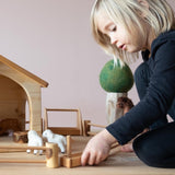 Ein Kind baut eine Weide für Bauernhof Tiere - mit einer kleinen Tränke aus Holz, Zäunen und einem Baunerhof.