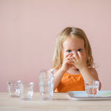Ein Mädchen trinkt aus einem kleinen Glas, perfekt zum Trinken lernen nach Pikler, perfekt zum Greifen mit den kleinen Händen.