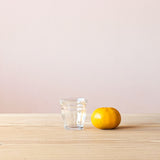 Ein Pikler Trinkglas für Kinder mit 13cl, daneben liegt eine Mandarine, sodass man einen guten Größenvergleich hat.