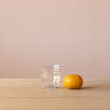 Ein Pikler Trinkglas für Kinder mit 16cl, daneben liegt eine Mandarine, sodass man einen guten Größenvergleich hat.