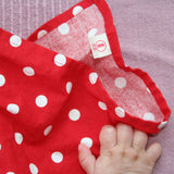 Eine Babyhand auf dem Pikler Tupfentuch in rot mit weißen Punkten. Das Etikett von Kokomoo ist zu sehen.