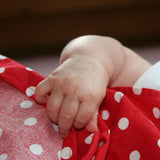 Eine Babyhand greift das Pikler Tupfentuch von Kokomoo, das rot mit weißen Punkten ist.