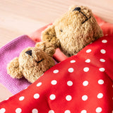 Zwei Kuschelbären schlafen zugedeckt unter dem roten Tupfentuch von Kokomoo, nur ihre Köpfe sind zu sehen.