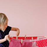 Auf dem Kinder Wäschständer von Glückskäfer hängen ganz viel rosa, pinke und rot-weiß getupfte Tücher, ein Kind befestigt gerade eine Wäscheklammer.