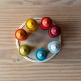 Die sieben Nins Holzfiguren vom Set Grapat 7 Moons stehen im Kreis in ihren sieben Holzbechern, auf einem flacher Holzteller.