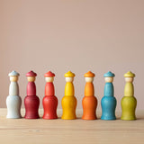 Die sieben Nins Holzfiguren vom Set Grapat 7 Moons stehen in einer Reihe auf den umgedrehten, passenden Holzbechern, von links beginnend mit Montag.