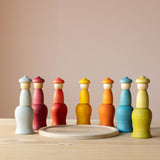 Die sieben Nins Holzfiguren vom Set Grapat 7 Moons stehen im Halbkreis auf ihren sieben Holzbechern, in der Mitte liegt ein flacher Holzteller.