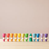 Die 12 "Wizards" Zauberer Spielfiguren aus Holz von Grapat stehen sortiert nach den Regenbogenfarben in einer Reihe, alle auf dem Kopf, bis auf dunkelgrün, der fünfte von rechts.