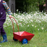 Der Schiebe- und Ziehwagen Ziehmichel von Lautenbach in rot wird von einem Kind hinter sich hergezogen durch eine Wiese.